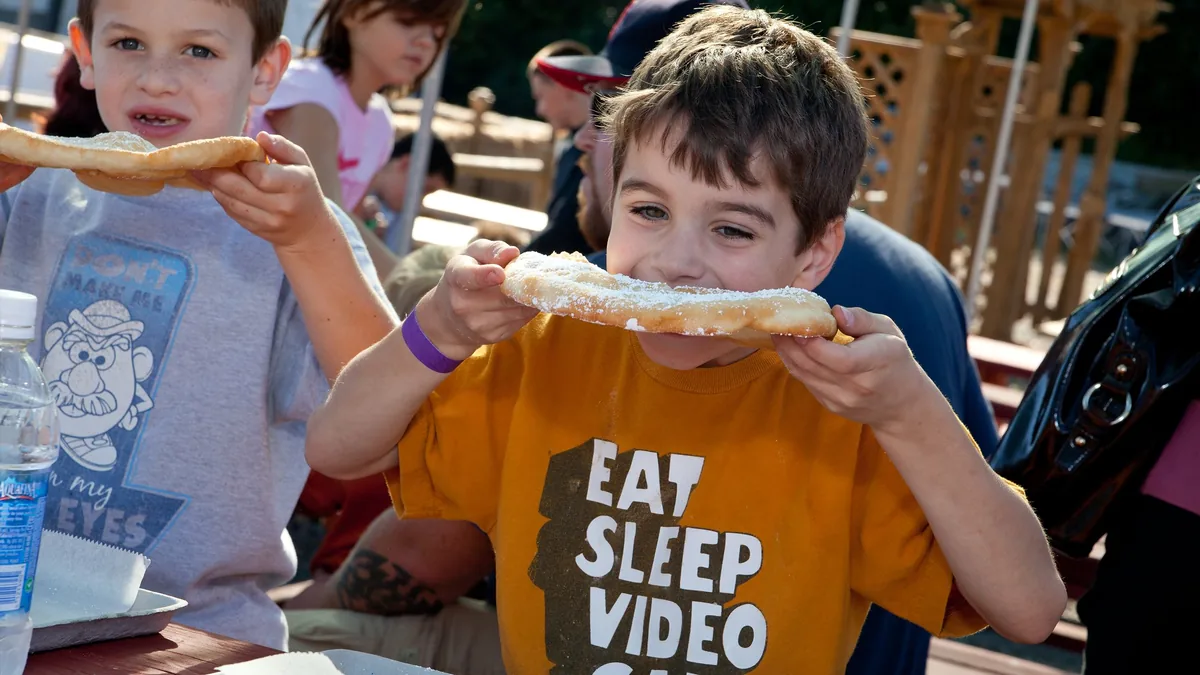 Two boys eating powdered-sugar fried dough at a picnic table